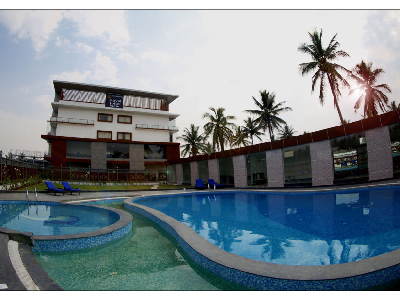 image of a beautiful swimming pool with clear waters surrounded by green trees situated in front of the resort building - Royal Lotus View Resotel