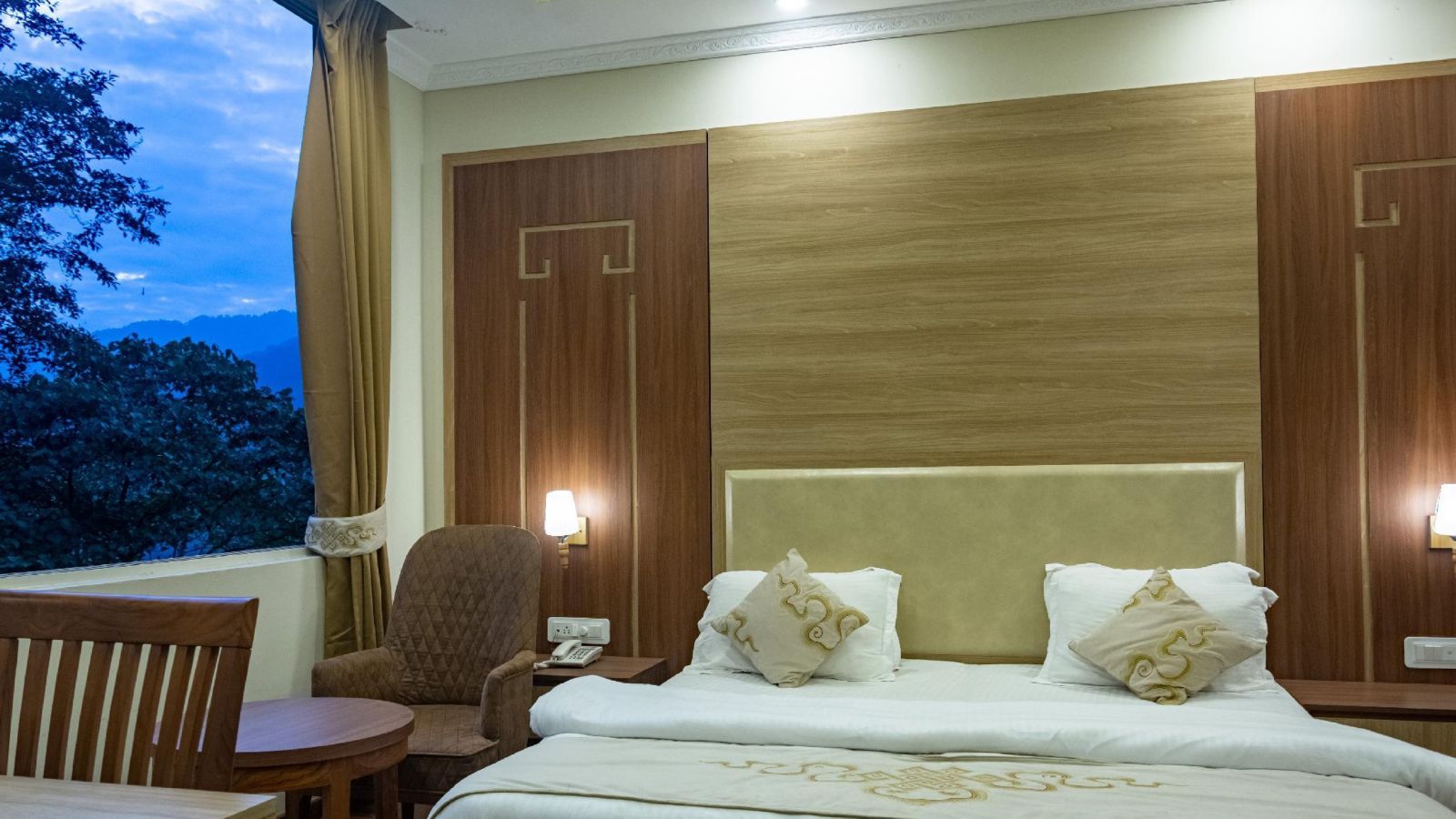 A queen bed with cushioned headboard and lamps on the side in Deluxe Room at Sumitel Gangtok ffak7i