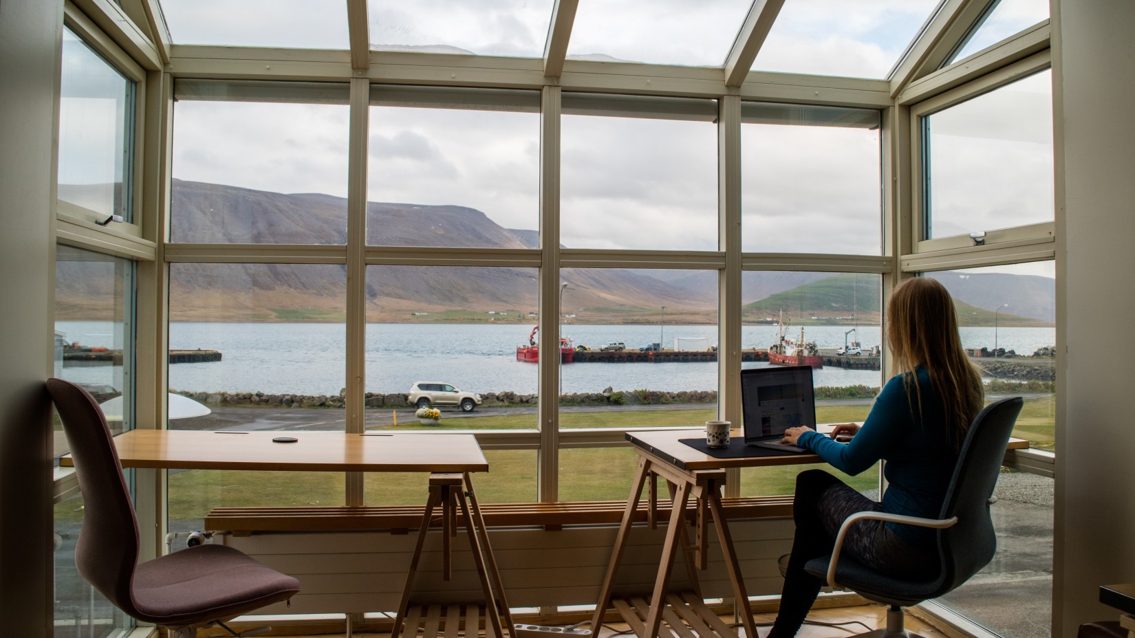 a person at work in a room overlooking mountains and a water body