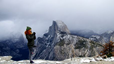 a woman performing a yoga asana on top of a mountain with snow on it and another mountain in the background