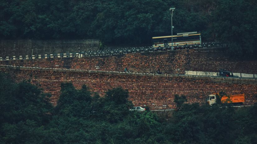 vehicles travelling on a hilly road in tirupati with lush green trees covering the foreground and background