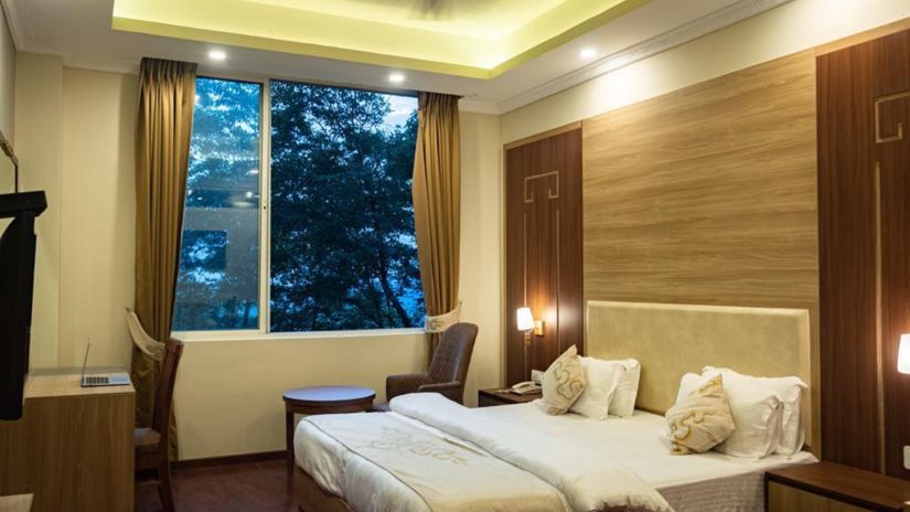 A queen bed with a large window next to it inside Deluxe Room at Sumitel Gangtok