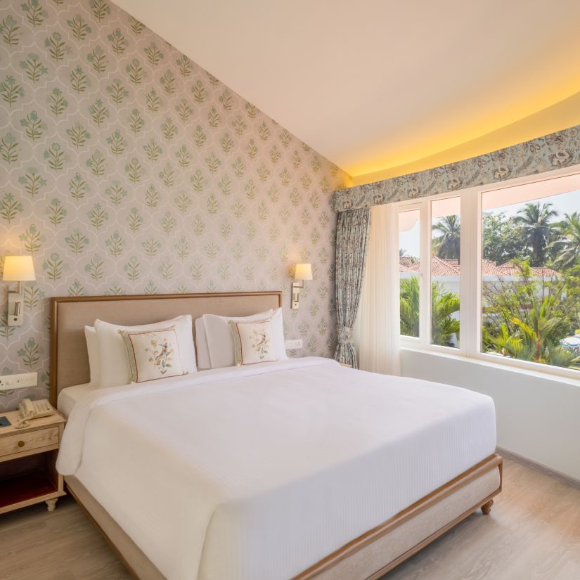 A double bed with side tables, lamps and pillows on the bed inside the suite - Heritage Village Resorts & Spa, Goa