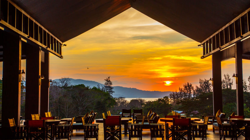 Wooden chairs in an open restaurant that overlooks a setting sun