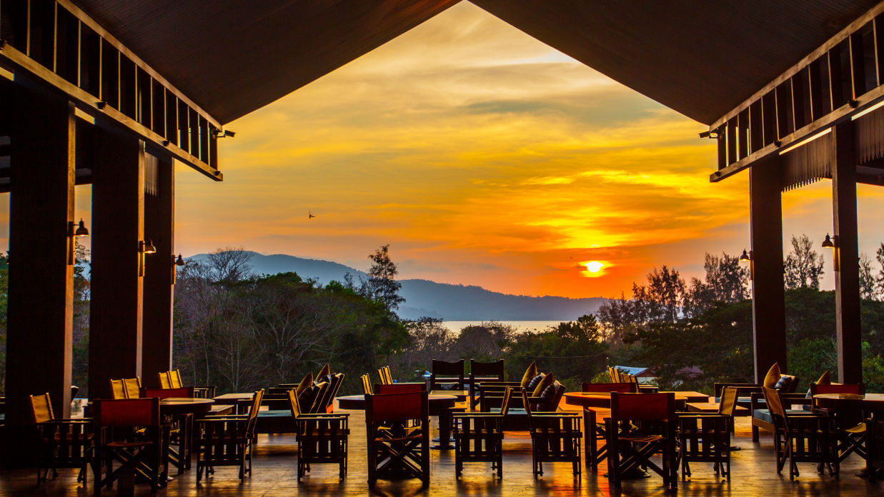 Wooden chairs in an open restaurant that overlooks a setting sun - Symphony Samudra Beachside Jungle Resort And Spa, Port Blair