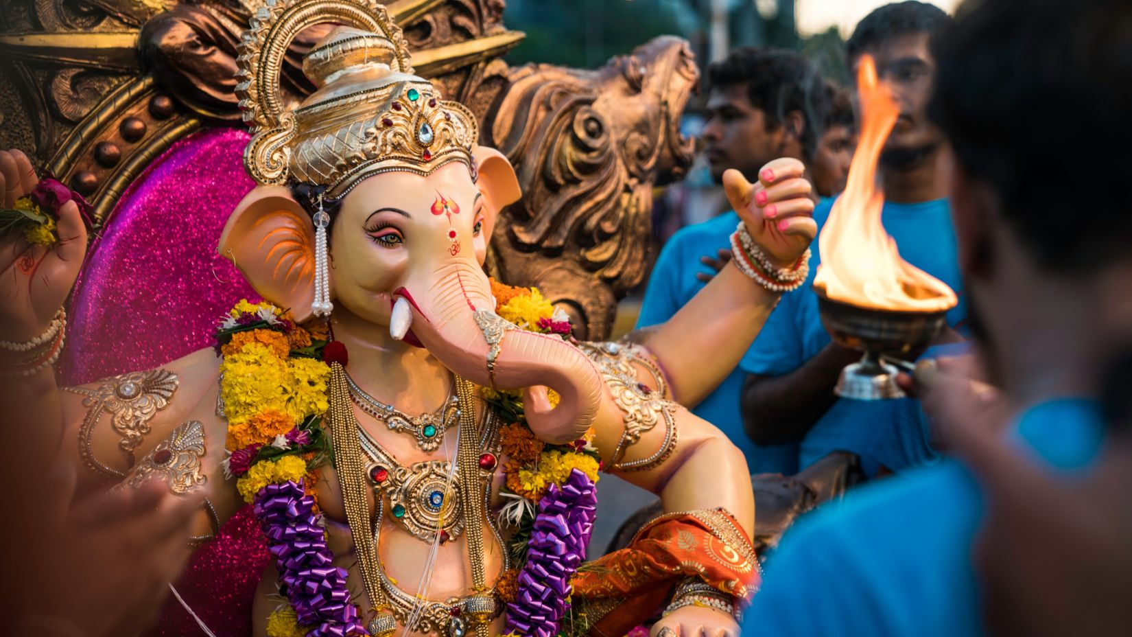 a person dressed as Ganesha dancing on the street with an arthi being performed on that person