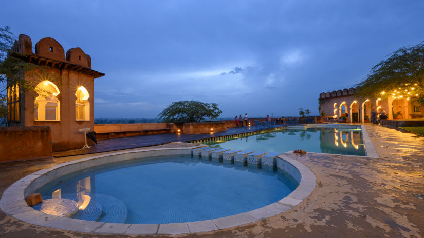 Hill Fort Kesroli 14th Century Alwar - view of two adjoined round swimming pools with an illuminated building structure in the background