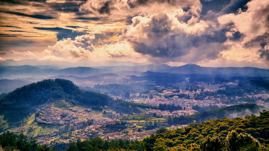 A dramatic view of a valley with terraced fields and a town under a cloudy sky