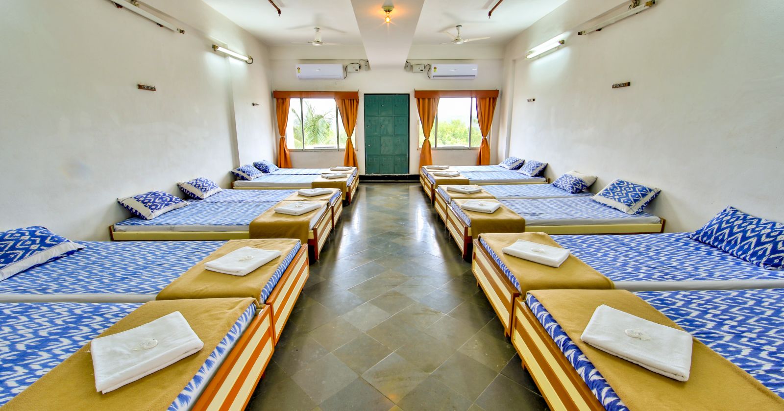 A full view of beds with bedding arranged in two rows in a room | Hotel Sahara