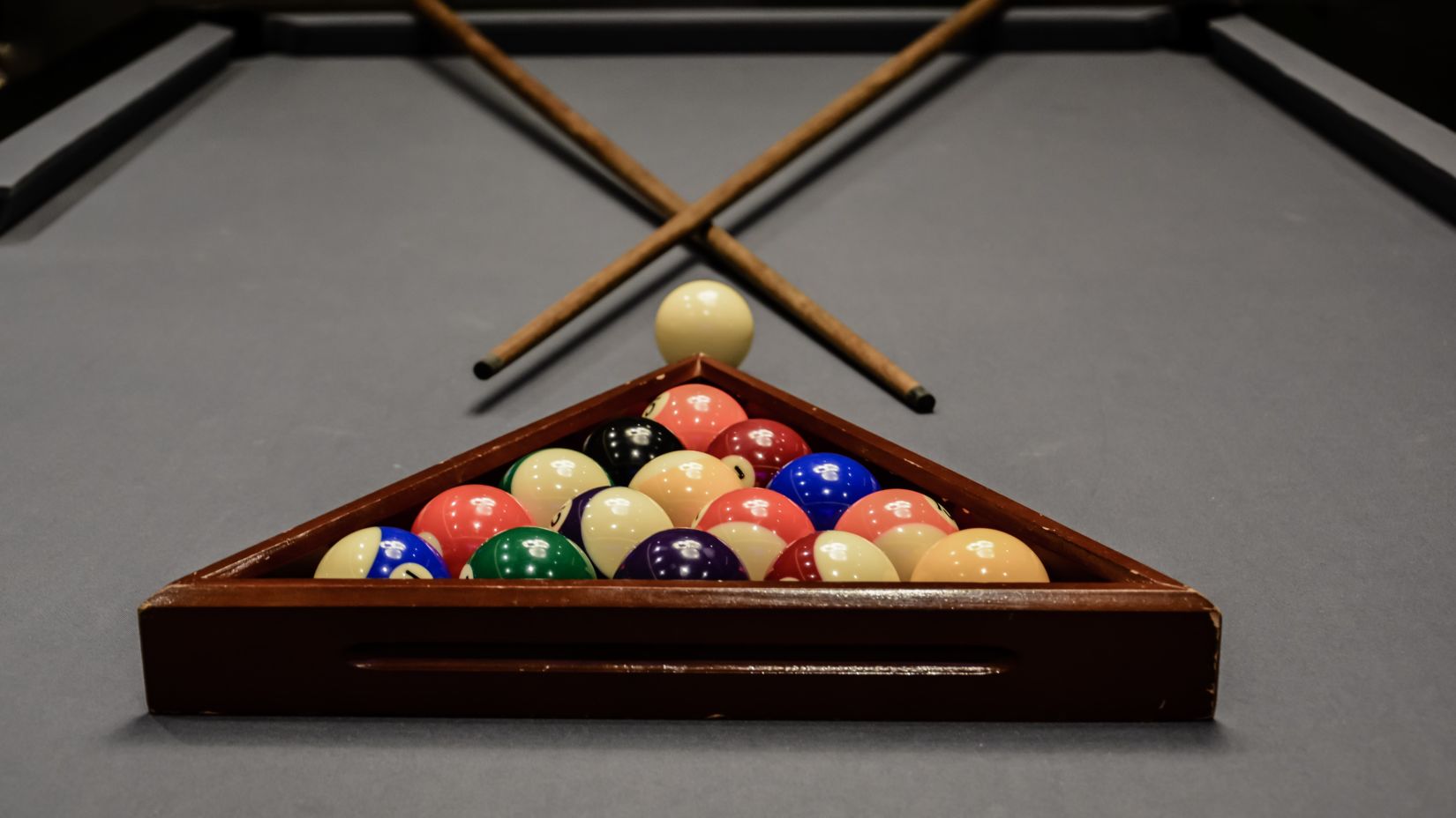 Pool balls being racked with two cues and a white ball on the table