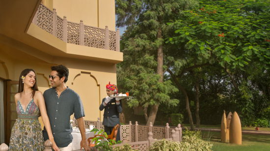 A couple posing in front of their romantic dinner with a butler carrying food behind them - Heritage Village Resort & Spa, Manesar