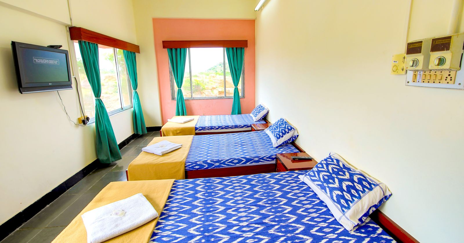 A sideview of three beds with bedding in a room with a window and TV | Hotel Sahara