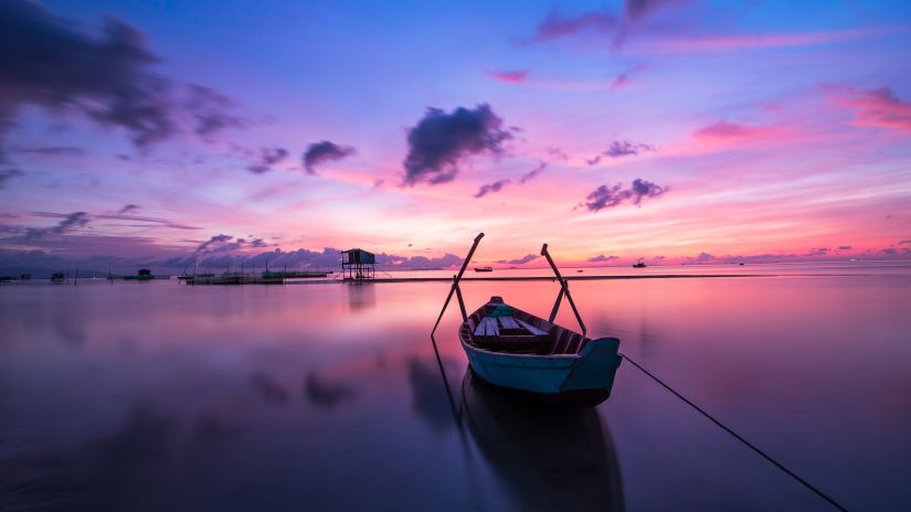 Boat anchored on calm waters with setting sun in background