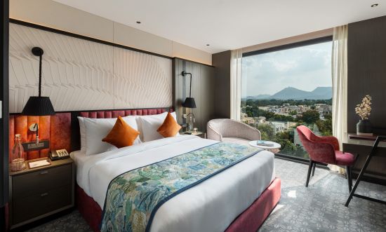 alt-text A spacious room with a large bed, full-length windows and a chair-table set - best boutique hotel in Udaipur, at Parallel Hotel Udaipur