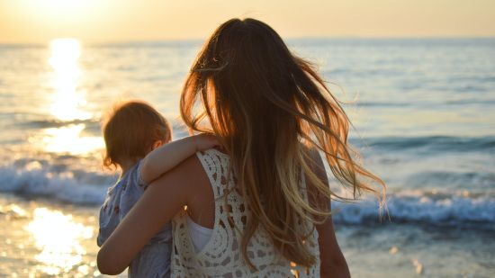 A woman holding a baby overlooks the beach during sunset - Varca Beach stay