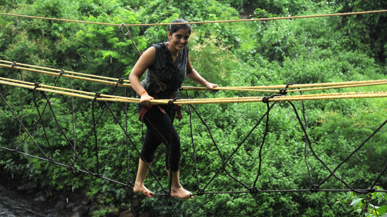 A focused individual crossing a rope bridge over a lush, green area. They appear determined, showcasing an adventurous outdoor activity.