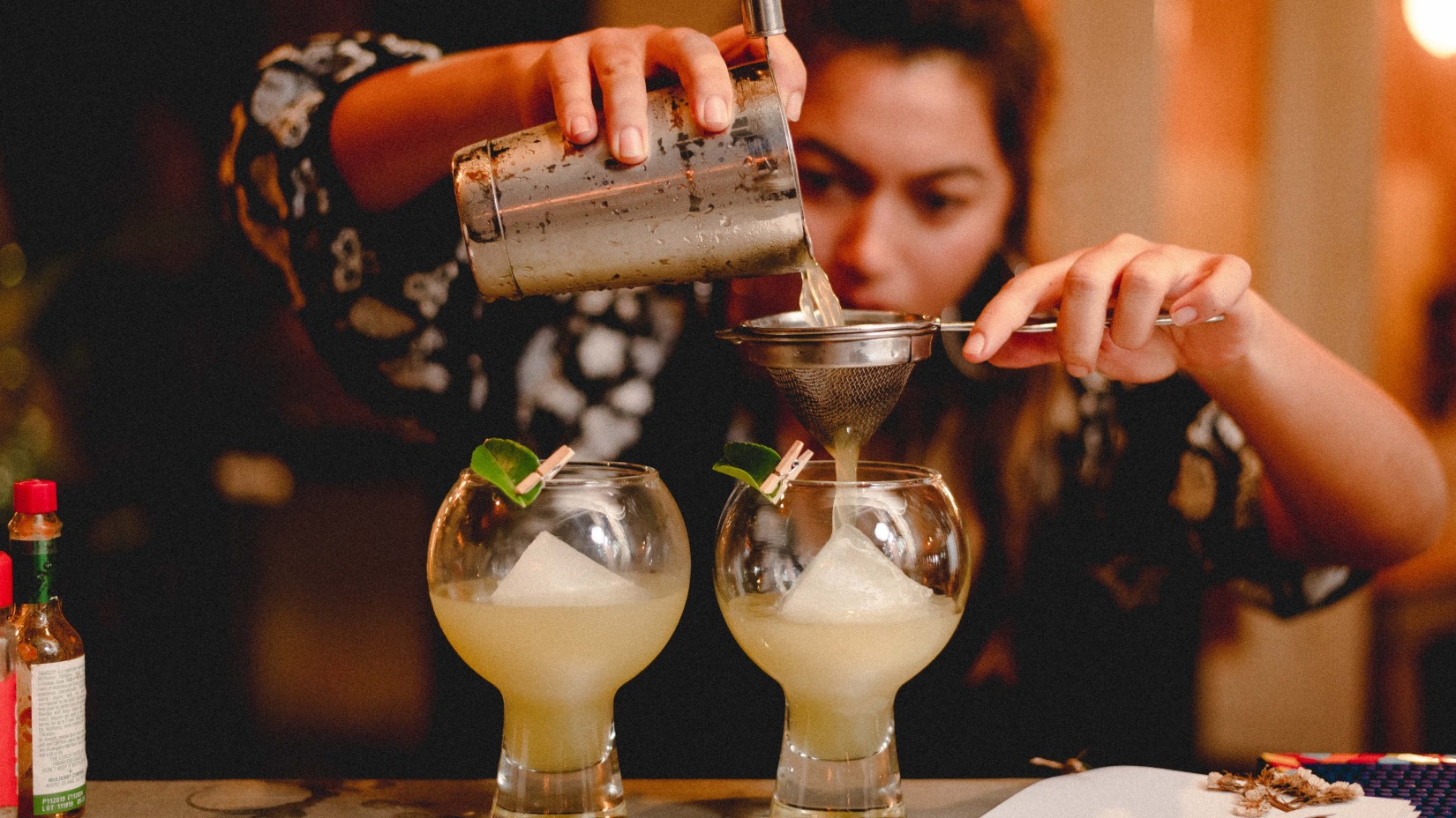 A woman carefully pours a drink through a filter into a glass - Villa in Palms by V Escapes