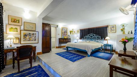 The Ramgarh Bungalows - a grand room with blue theme, featuring a work desk and wall paintings along with room amenities like an electric kettle, fruit basket, bedside lamp, etc.