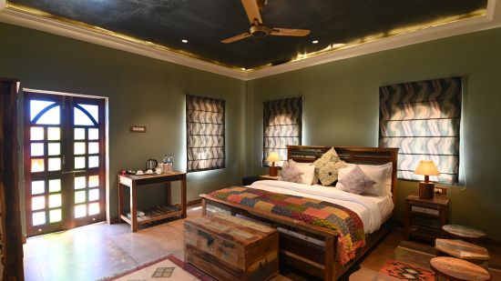 The bedroom of the Luxury Cottage offers a spacious bed surrounded by dark green walls - Karwaan Jaisalmer