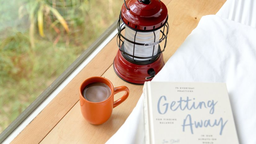 a cup of coffee next to a book and lantern