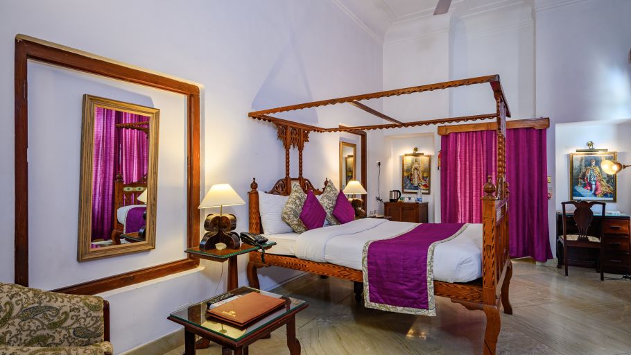 An overview of the Rani Fateh Kaur room with a double bed, mirror, and side tables - The Baradari palace