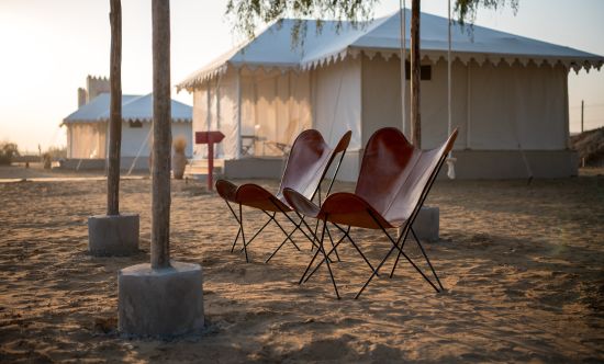 alt-text Foldable chairs are placed on the sand near the accommodations - Karwaan Jaisalmer