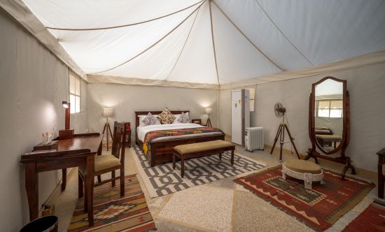 alt-text The interiors of the accommodations contain a spacious bed, work desk and other amenities - Karwaan Jaisalmer