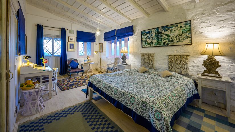 The Ramgarh Bungalows - a blue themed grand room with work desk and a fruit stand next to it, featuring a king size bed and night lamp