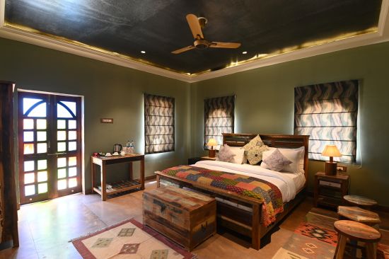 alt-text The bedroom of the Luxury Cottage offers a spacious bed surrounded by dark green walls - Karwaan Jaisalmer