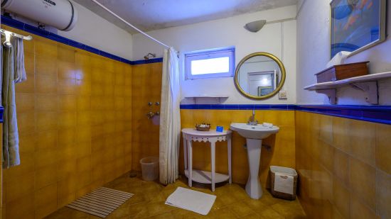 The Ramgarh Bungalows - a white & yellow themed bathroom with water heater on the left and shower space beside