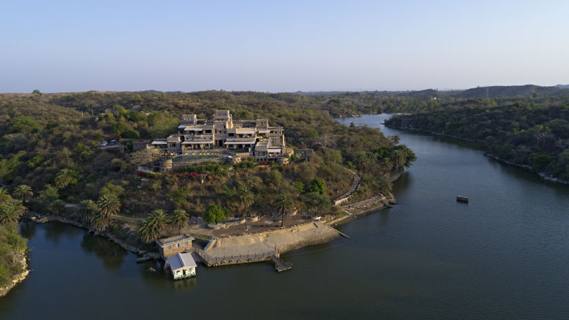 aerial view of Chunda Shikar Oudi, Udaipur with a forest covering the resort and lake surrounding the forest