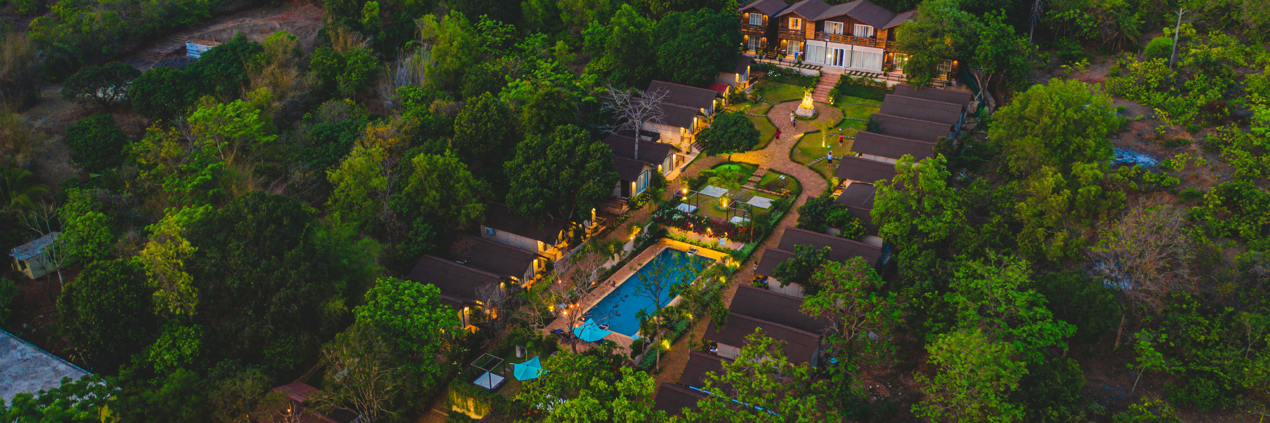 aerial view of a resort located amidst green trees featuring a pool and decorated with aesthetic yellow lights  aerial view - Stone Wood Hotels & Resorts2