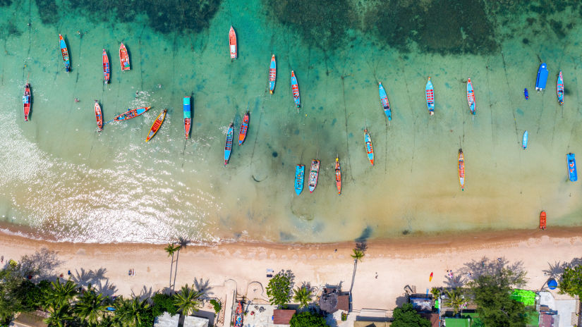 aerial view of long tail boats and a group of people on the beach