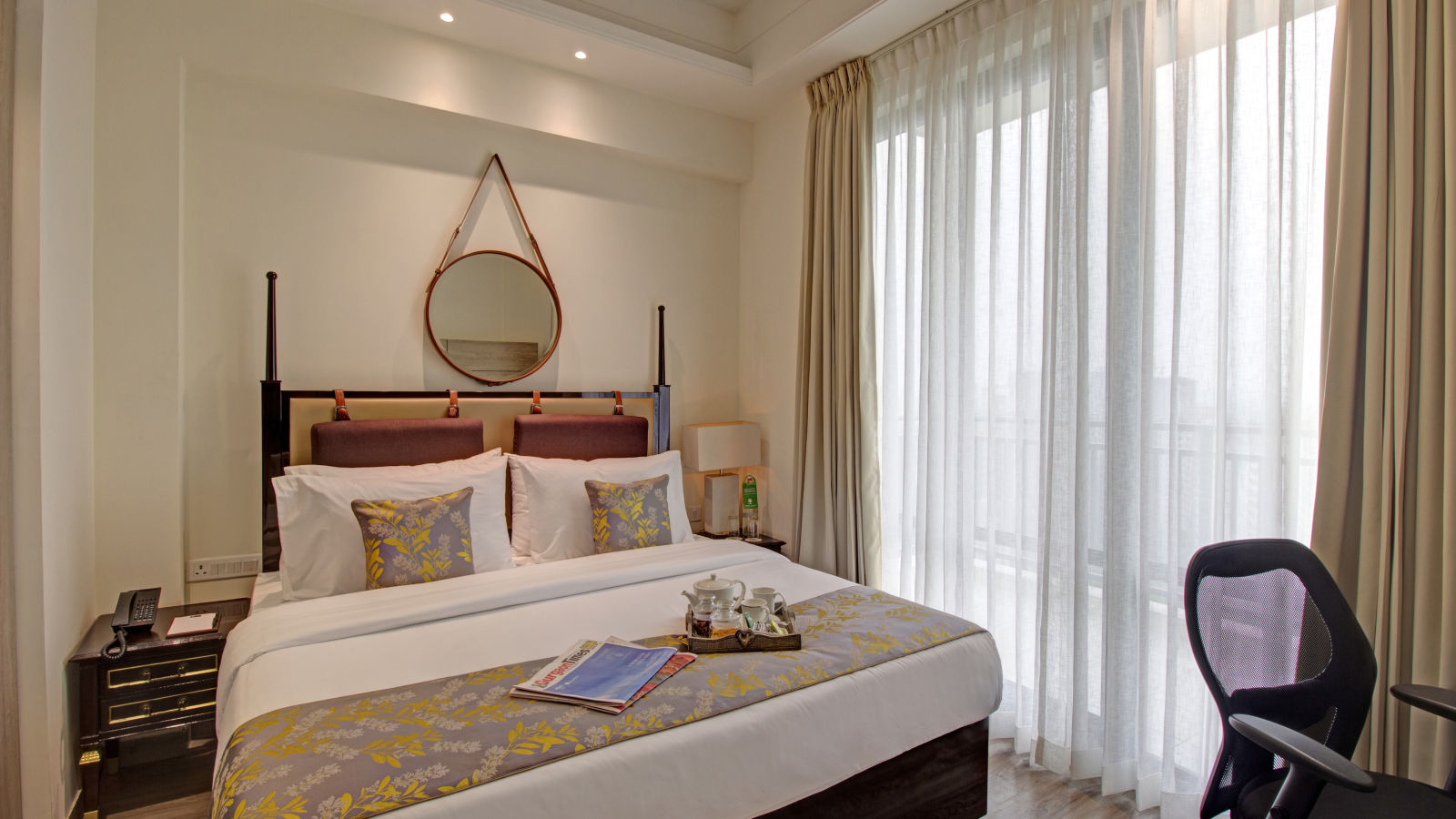 a king bed with side tables and a study desk opposite the bed inside Deluxe Suite at Rhythm Gurugram