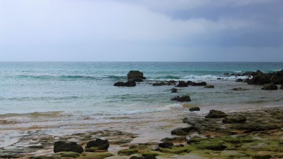 A view of a beach with rocks and dark skies in the background