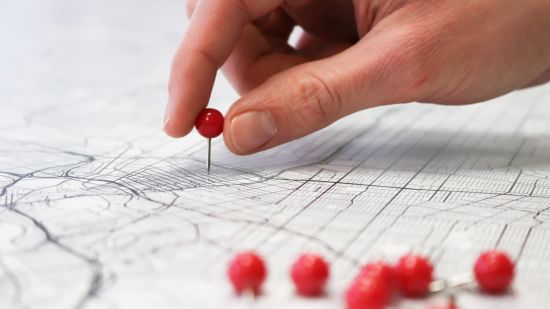 a person putting red pin on a map with other pins on the side