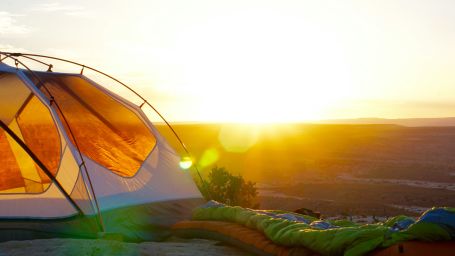 View of a tent with a sleeping bag beside it and a bright sunrise in the background