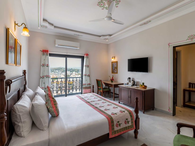 An overview of the suite with a king bed, tv and balcony at Superior Room - Maan Vilas by Stone Wood, Udaipur