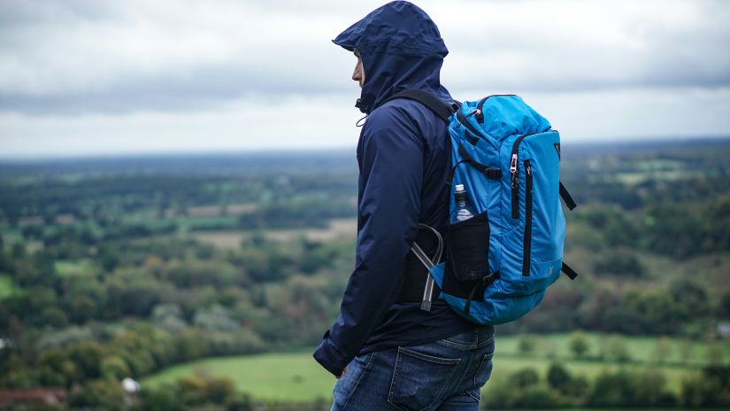A man with a blue backpack gazes out over a lush green landscape from the viewpoint.
