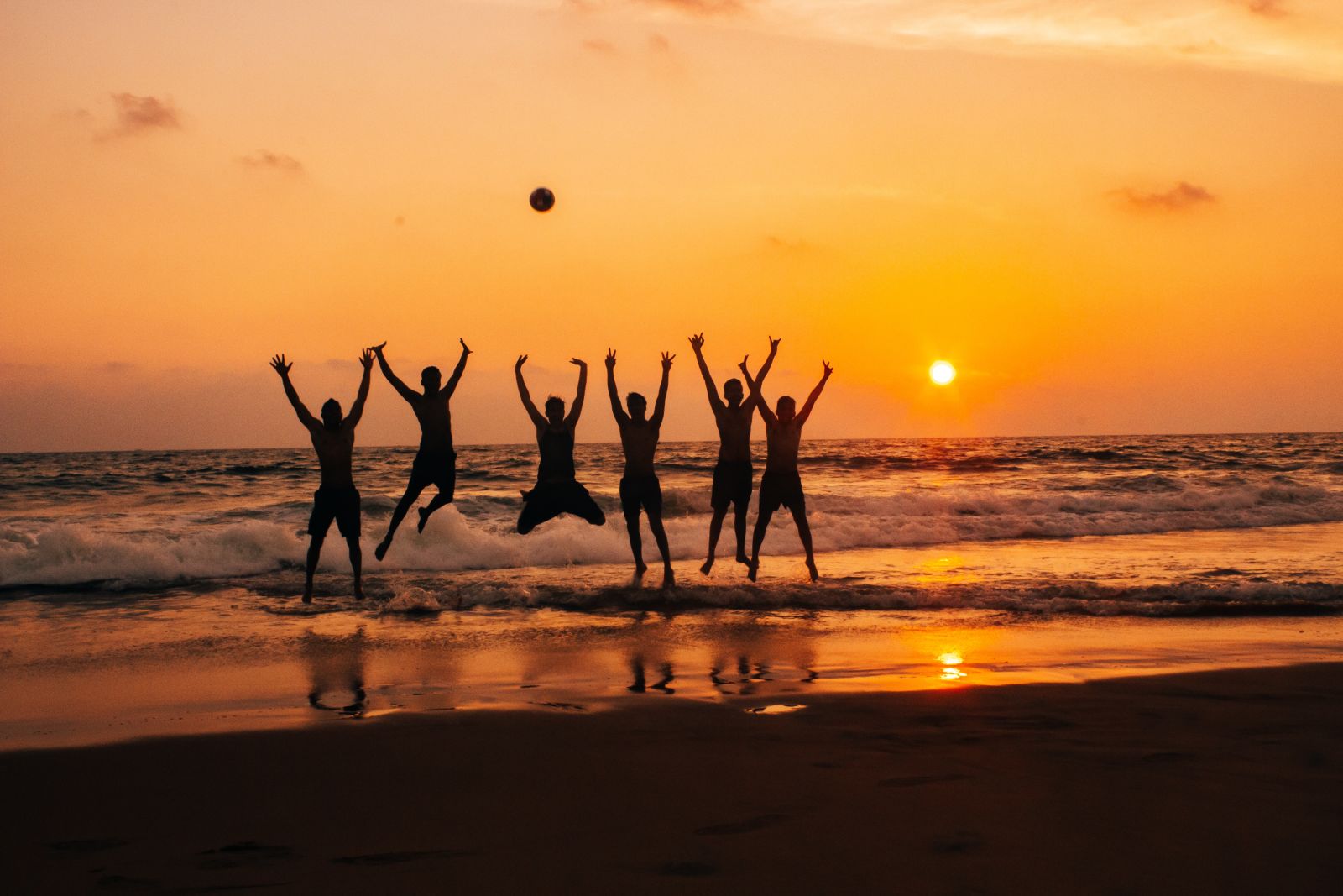 Six men jump on the shore in unison as the sun sets behind the beach waters - best honeymoon places in Kerala