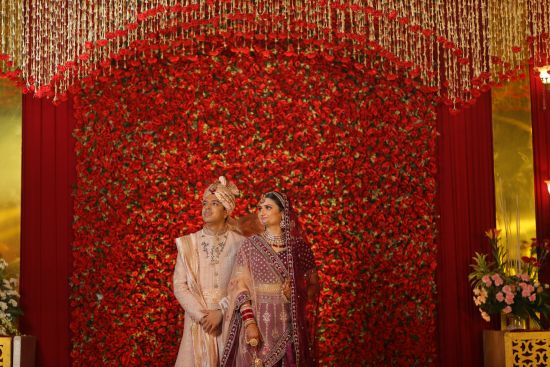 alt-text bride and groom posing for pictures with a backdrop of red - heritage village resorts & spa, Manesar