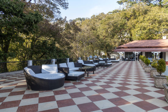 alt-text An outdoor seating area at The Claridges Nabha Residence in Mussoorie, characterized by comfortable, plush seating and encircled by a dense, lush green forest.