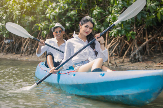 alt-text Two individuals, each in a kayak, paddling through calm river waters surrounded by dense mangroves, showing a peaceful and serene exploration setting.