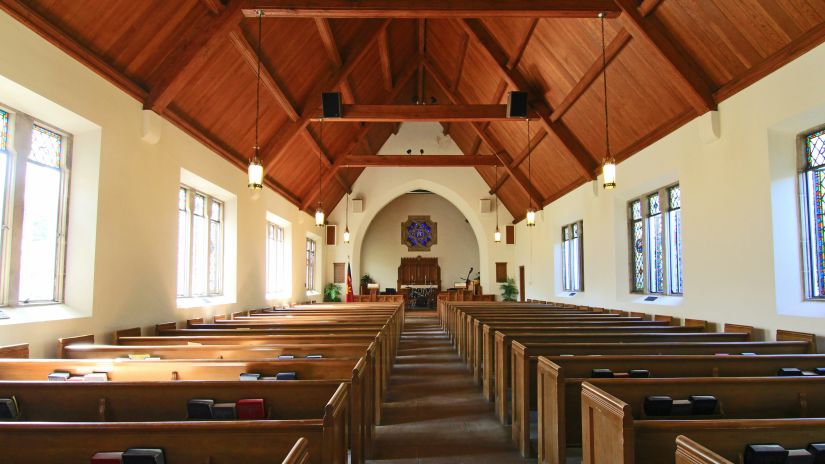 A church interior with wooden pews and stained glass windows.