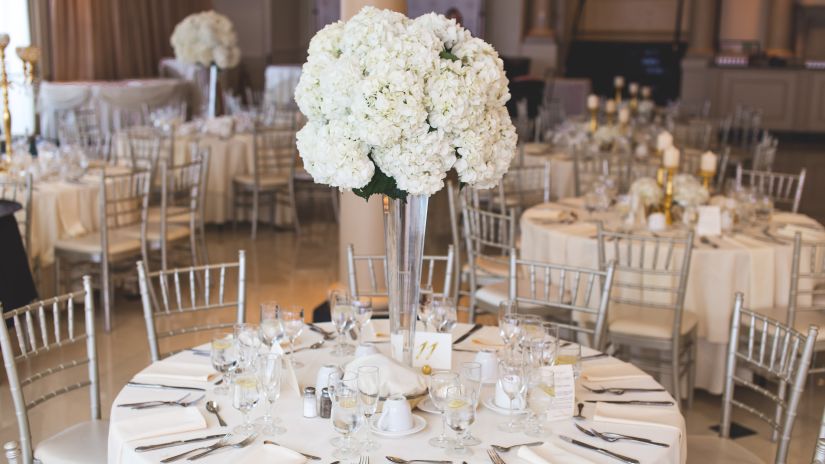 Our best Banquet hall in Udaipur and event hall with silver chairs and white cloth covered centre table along with beautifully kept bouquet