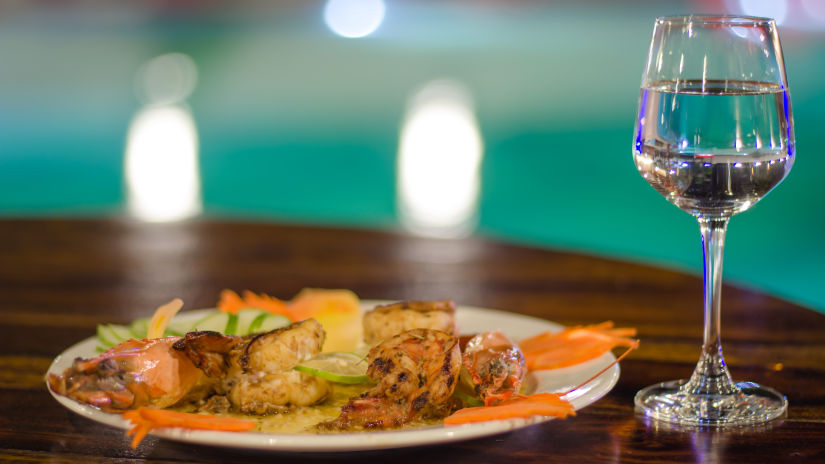 glass of water next to plate of food kept on a table with the swimming pool in the background - Symphony Summer Sand Beach Resort And Spa, Neil island