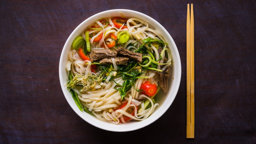 a bowl of noodle soup garnished with vegetables with a chopstick on the side