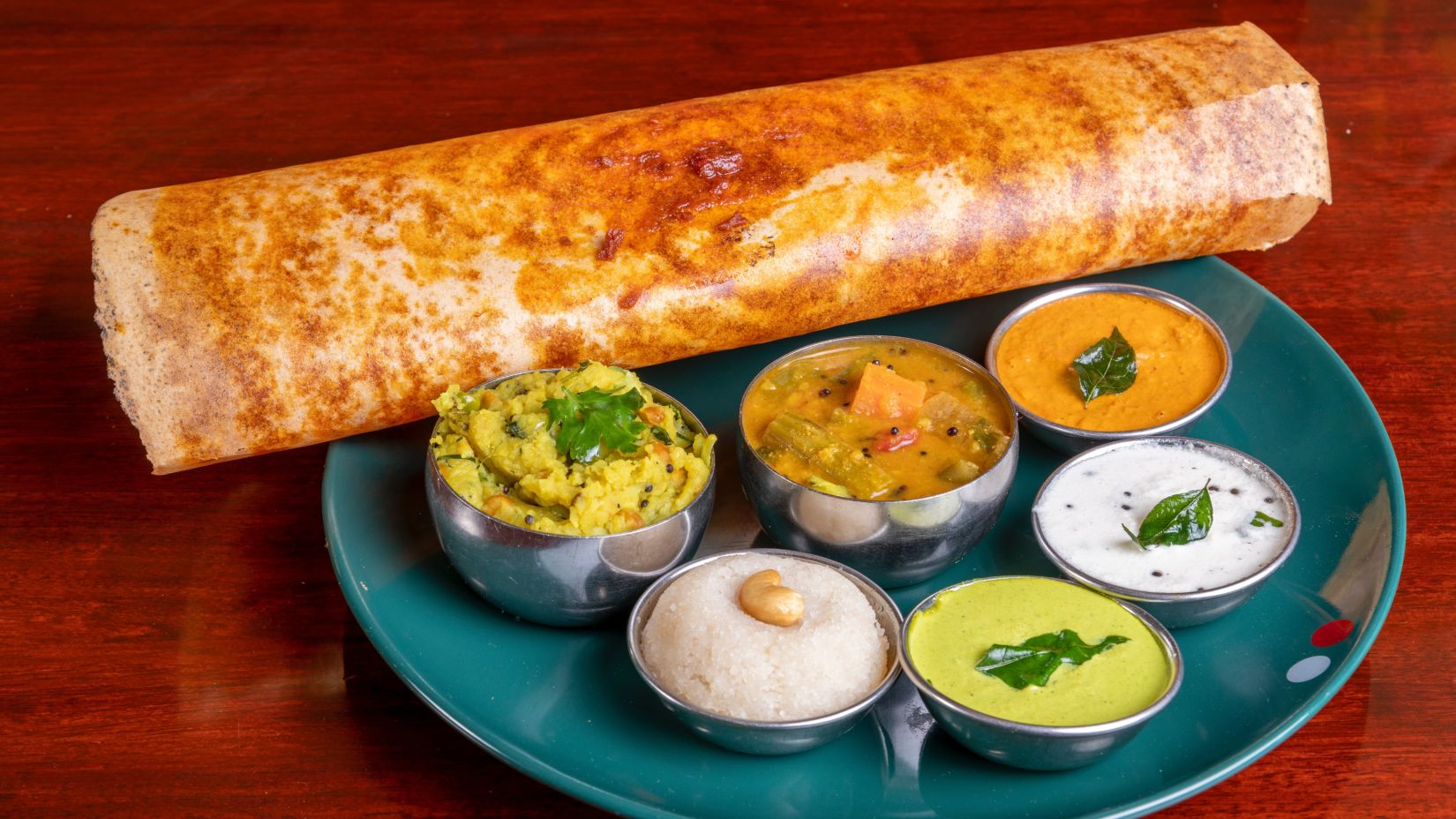 a plate served with a brown dosa and other side dishes