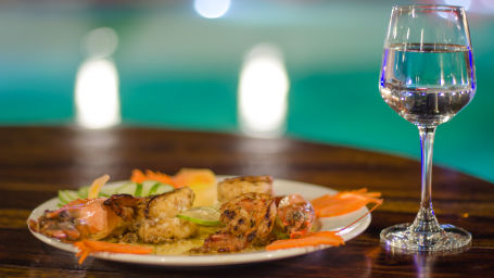 glass of water next to plate of food kept on a table with the swimming pool in the background - Symphony Summer Sand Beach Resort And Spa, Neil island