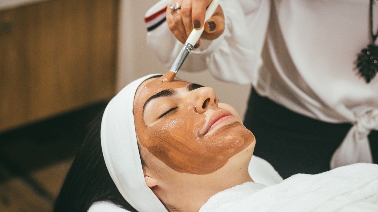 a person applying face mask on a woman's face during spa